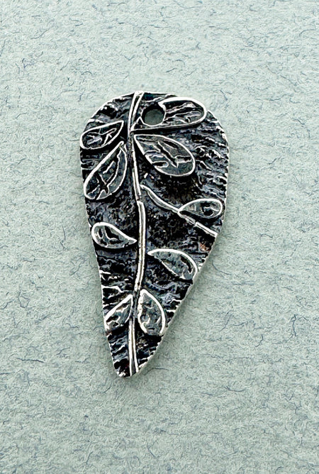 Silver leaf-shaped pendant on a light gray textured background