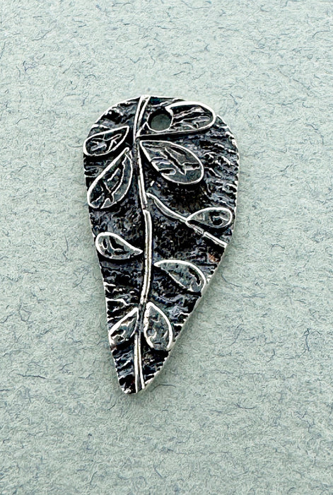 Silver leaf-shaped pendant on a light gray textured background